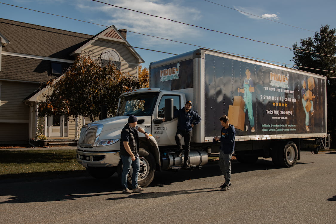 Move and Care movers standing beside a branded box truck outside a suburban home