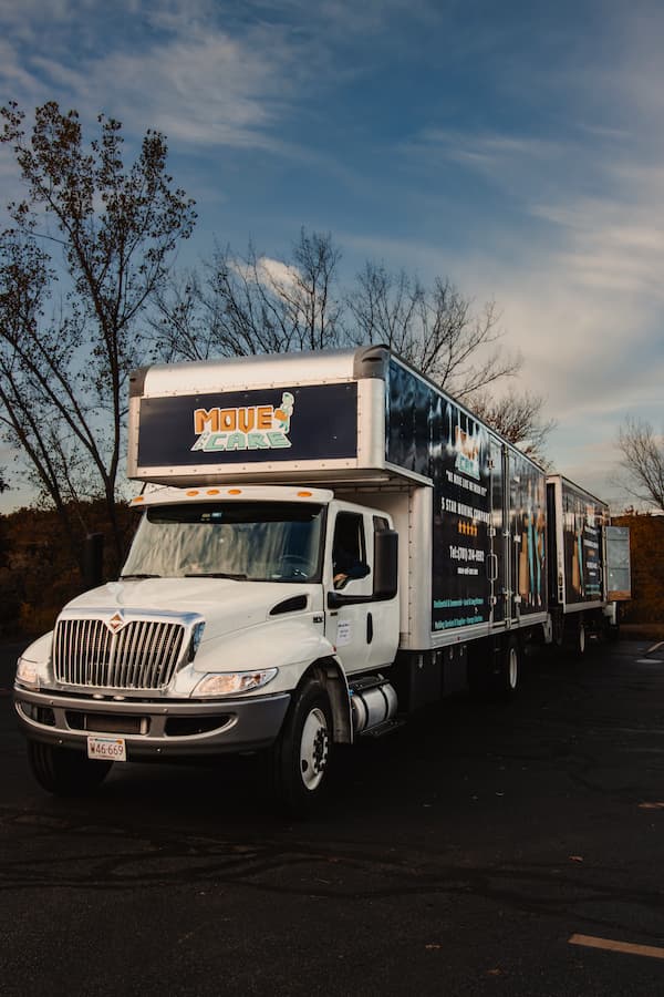 Move and Care long-distance moving truck with a box trailer at dusk
