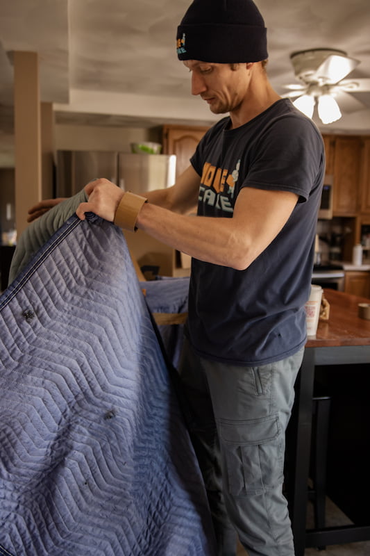 Move and Care mover wrapping furniture in a padded moving blanket